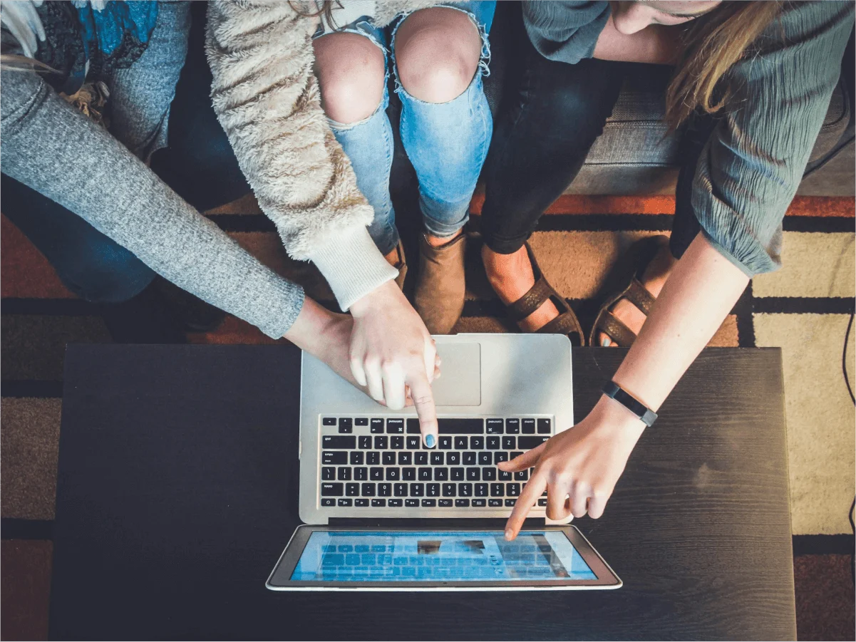 Three people sitting on a couch pointing at a laptop.
